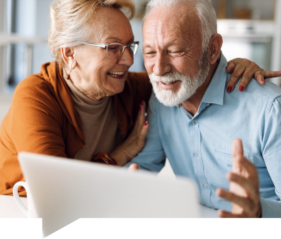 Retired foster carers looking at a laptop and smiling